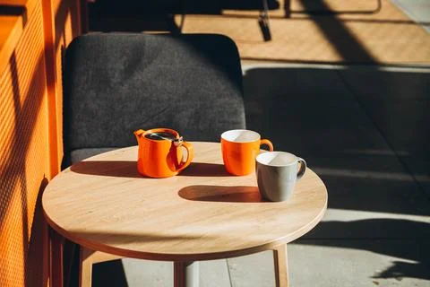 Two cups and a teapot on a table in a cafe with hard shadows. Stock Photos