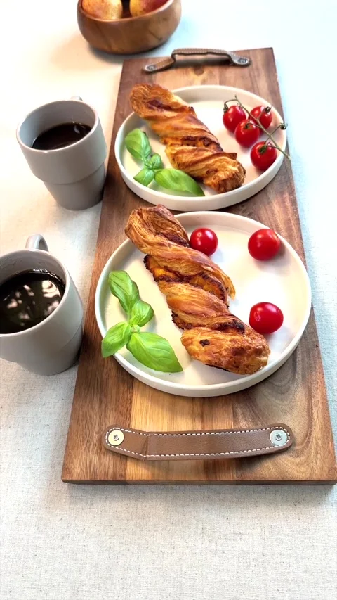 Two cups of black coffee paired with golden pastries, basil, and bright cherry Stock-Footage 291690154