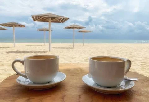 Two cups of coffee against backdrop of sea beach Stock Photos
