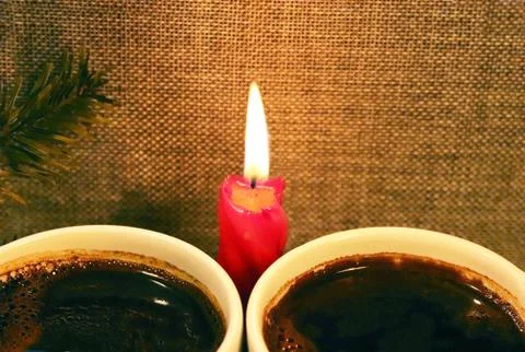 Two cups with coffee on the background of a red candle and a sprig of spruce. Stock Photos