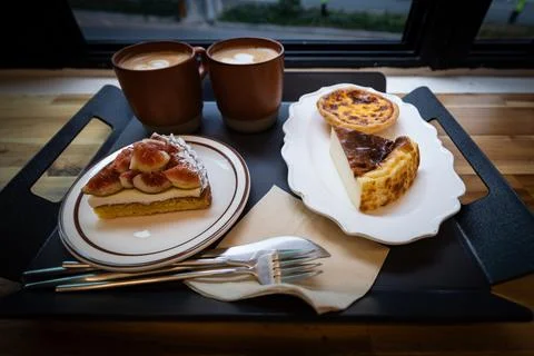 Two cups of coffee, cheese cake and figs tart on the tray in coffee shop Stock Photos