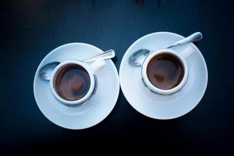 Two cups of coffee with round white plates and tea spoons on black table. View 写真素材