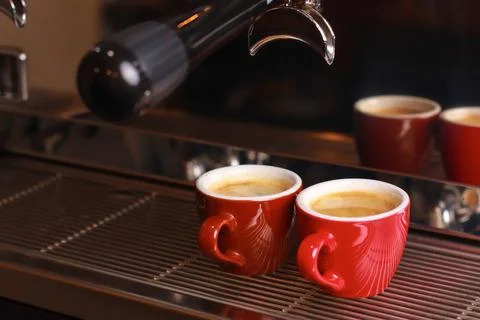 Two cups of coffee stand on the grill, coffee with foam poured from the coffee Stock Photos