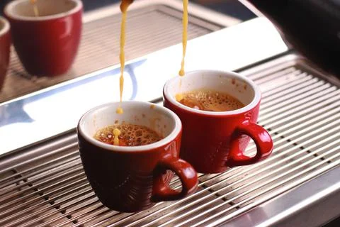 Two cups of coffee stand on the grill, coffee with foam poured from the coffee Stock Photos