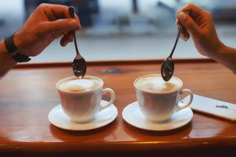 Two cups of coffee on the table, man's hand and a woman's hand with spoons. Foto stock