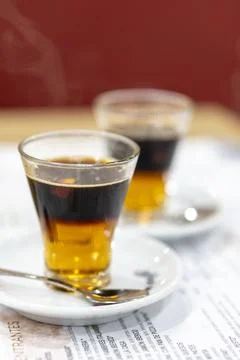 Two cups of coffee on a white plate with a spoon in between them Stock Photos