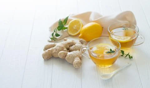 Two cups of healthy ginger tea with mint leaves and lemon on white table Stock Photos