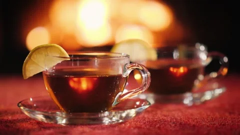 Two cups of hot tea with lemon slices in front of fireplace warm glow, cozy.. Stock Footage 334591579