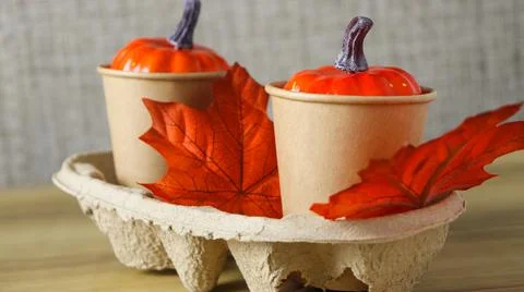 Two cups with orange pumpkins and red leaves in an egg carton display with a Stock Photos