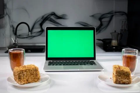 Two cups of tea and two pieces of cake in gray kitchen next to laptop with green Foto stock