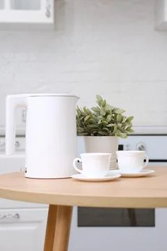 Two cups of tea and white electric kettle, green flower in pot on wooden round Stock Photos