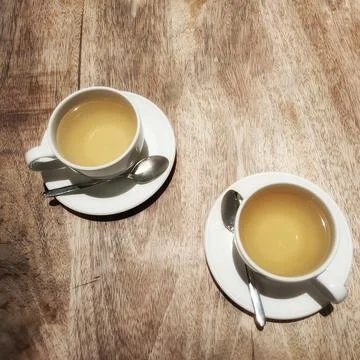 Two cups of tea are on white saucers on a wooden table. Stock Photos