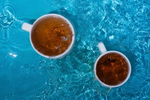 Two cups of tea in blue splashing water Stock Photos