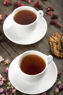 Two cups of tea, flowers and oatmeal biscuits on wooden background Stock Photos