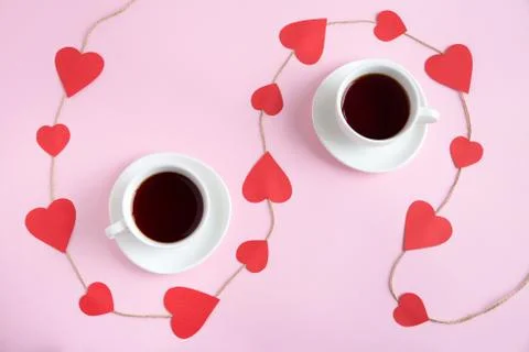 Two cups of tea on pink background with cord decorated with paper red hearts.  Foto stock