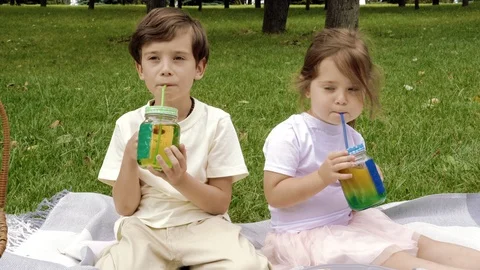 Two cute children drinking juice using a straws outdoors Stock Footage 111947683