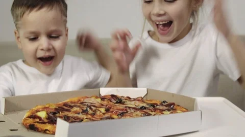 Two cute children in white t-shirts, a boy and a girl open a box of pizza and Video stock 103570911