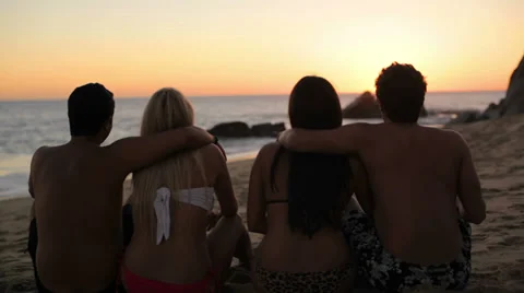 Two cute couples sit on the beach and watch the sun go down in Mexico Stock Footage 33876162