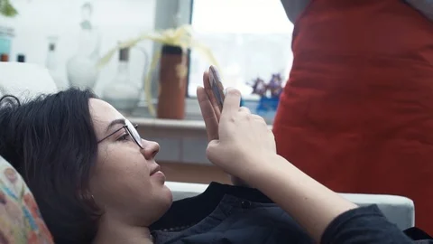 Two cute girls laughing using smartphone lying on couch at home. Video stock 87065050