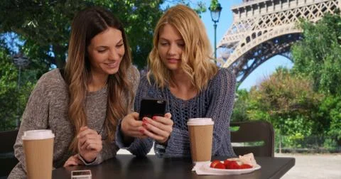 Two cute girls using cell phone to look at pictures near Eiffel Tower Stock Photos