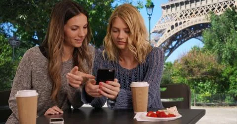 Two cute girls using cell phone to look at pictures near Eiffel Tower Foto stock