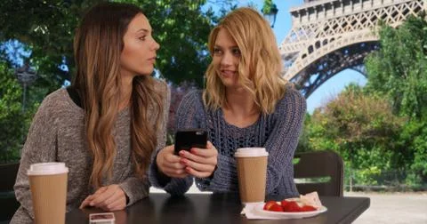 Two cute girls using cell phone to look at pictures near Eiffel Tower Foto stock
