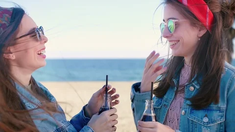 Two cute Hispanic sisters standing and drinking lemonade on the beach, enjoy Video stock 106194905
