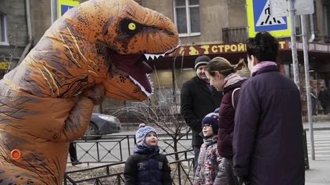 Two cute kids talking to person in dinosaur costume at sidewalk Stock Footage 84930880