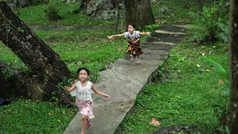 Two cute sisters running together on a stone path in a botanical garden. Stock Footage 241980116