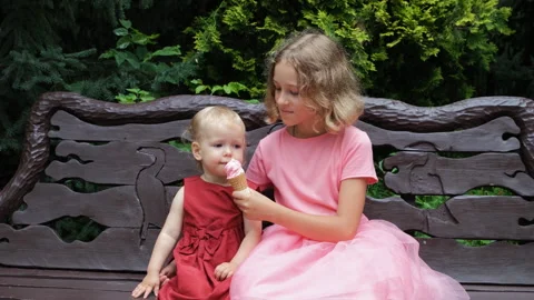 Two cute sisters share a ice cream cone on bench Stock-Footage 283928843