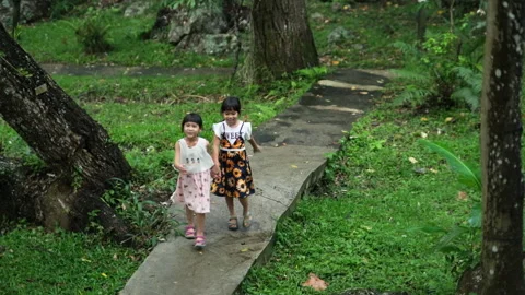 Two cute sisters walking hand in hand on a stone path in a botanical garden. Stock Footage 241979914