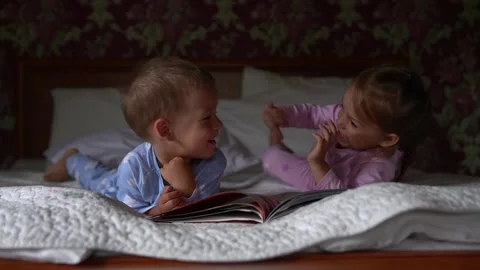 Two cute smiling preshool, toddler children on pajamas read book of fairy tales Video stock 156938099