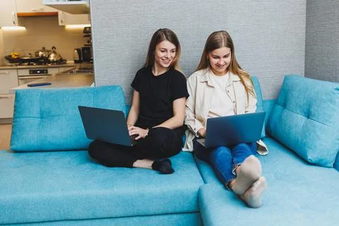 Two cute women working using laptop in living room on sofa. Friends, friendsh Stock Photos