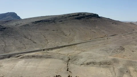 Two cyclists ascend a paved road cutting through the desert under a black ridge. Stock Footage 127019891