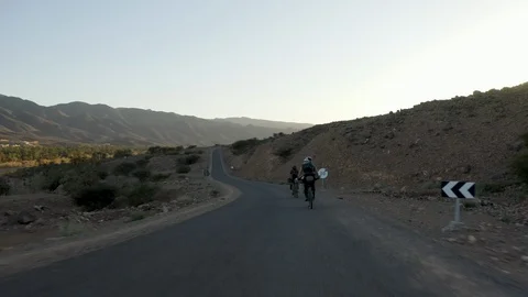 Two cyclists coast downhill on a paved road through dry, desert terrain. Stock Footage 127020441