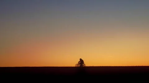 Two cyclists cycling in medium tempo on flat hill at glowing sunset Stock Footage 251488358