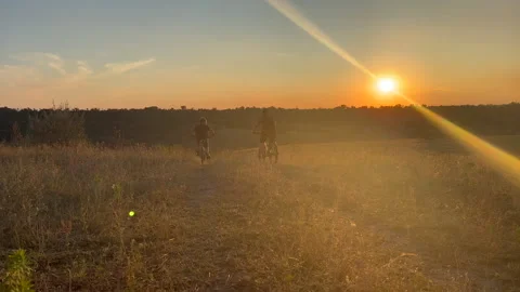 Two cyclists leave along the sunset road. two brothers on bikes at orange sunset Stock Footage 247134698