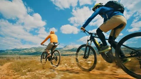 Two cyclists race through a mountain trail under a blue sky Foto stock