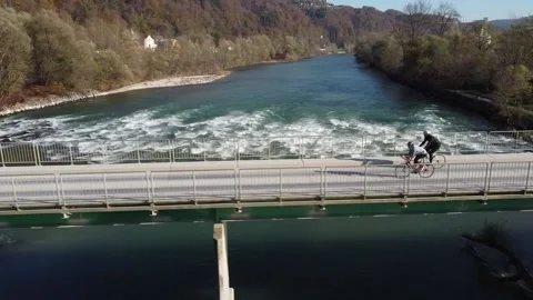 Two cyclists ride across the bridge over rough river Stock Footage 143362207