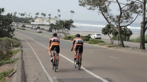 Two Cyclists Ride Down a Hill Near The Ocean Slow Motion Stock Footage 108746506