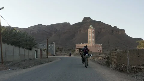 Two cyclists ride past a mosque as a woman in a burka passes by. Stock Footage 127020231