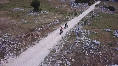 Two Cyclists ride on a path in an open mountain valley, aerial view Stock Footage 112994452