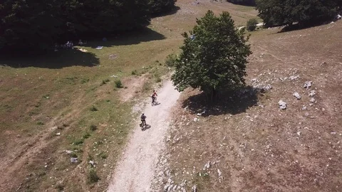 Two Cyclists ride on a path in an open mountain valley, aerial view Stock Footage 113040583