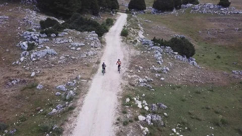 Two Cyclists ride on a path in an open mountain valley, aerial view Stock Footage 113040596