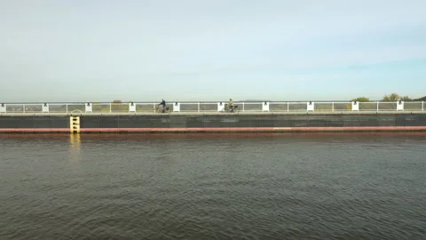 Two cyclists ride from right to left  over a trough bridge 스톡 동영상 219893602