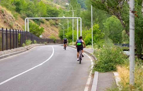 Two Cyclists Riding Down a Winding Road in a Green Valley Stock Photos