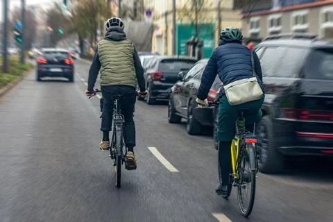 Two Cyclists Riding Through City Traffic During Commute Stock Photos