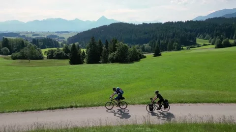 Two cyclists rolling downhill in a green landscape with mountains Video stock 198146165