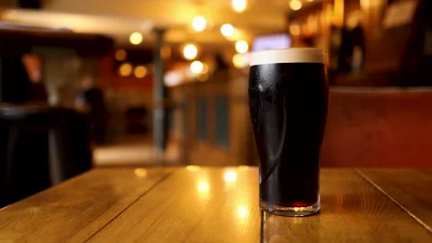 Two dark beers with frothy heads sit on a wooden table inside a cozy pub wi.. Stock Footage 333432008
