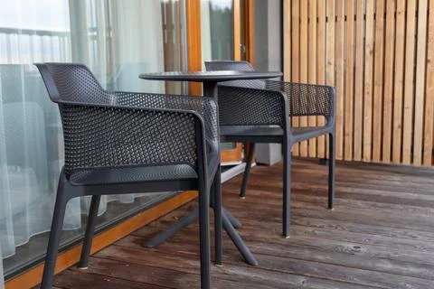 Two dark plastic perforated armchairs and a small round table on a wooden Stock Photos